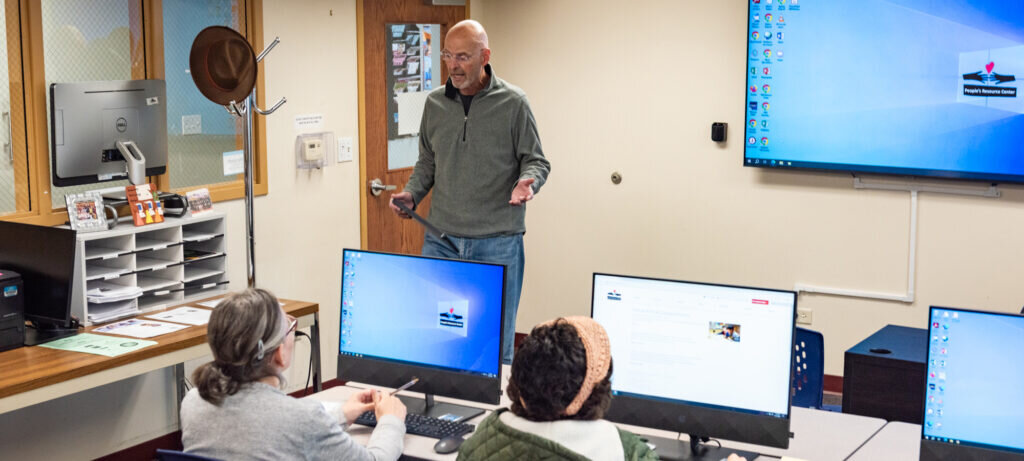Man standing in front of people in a classroom teaching a computer training class