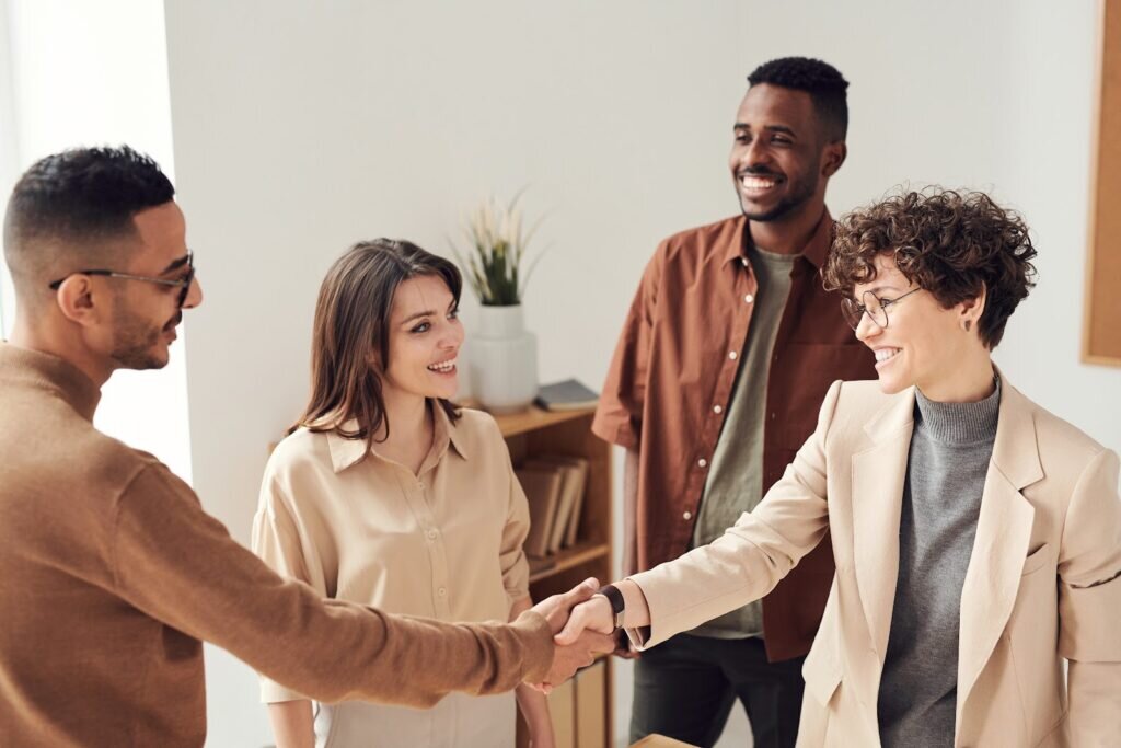 A man and woman shake hands and smile while two other people watch and smile