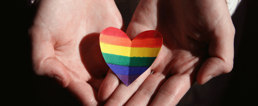 Hands holding a paper rainbow heart