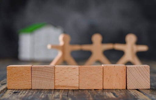 Family safety concept with wooden figures of people, cubes, model house on wooden and foggy background side view.